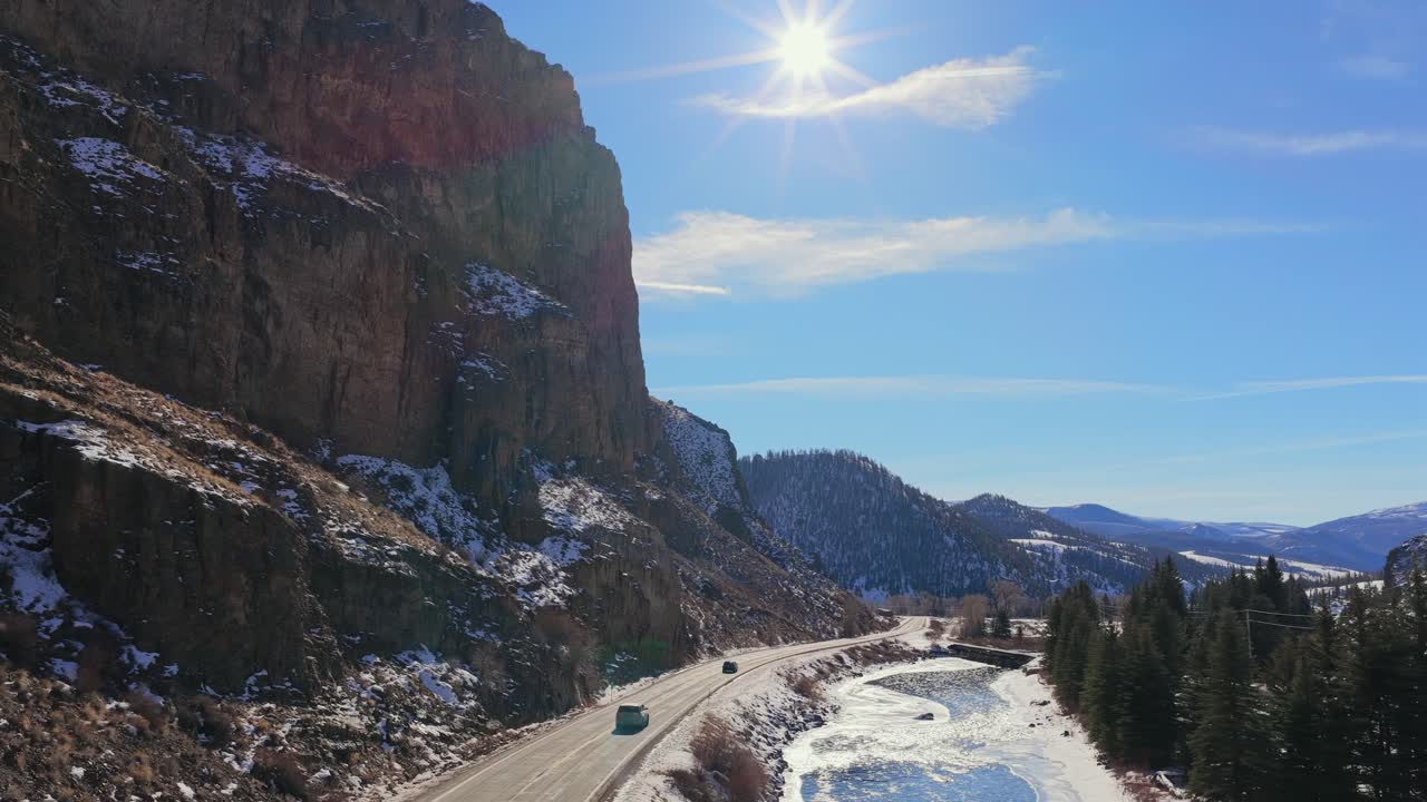 Un'inquadratura aerea cinematografica segue un SUV blu lungo una tortuosa strada di montagna con un lens flare. Questa scena invernale è ideale per spot pubblicitari di auto, vlog di viaggio e narrazioni di avventure