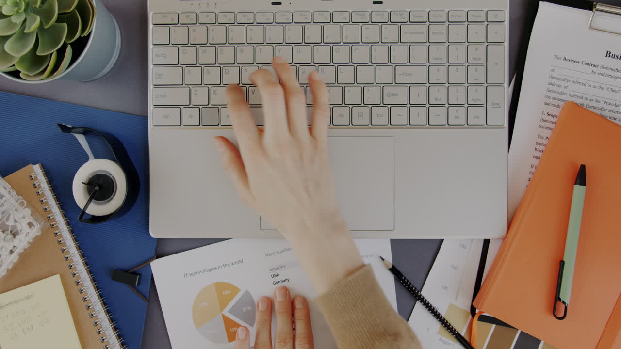 Person arbejder på en bærbar computer med dokumenter og diagrammer