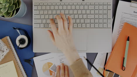 Person Working on a Laptop with Documents and Charts