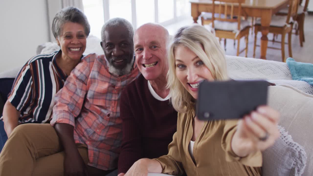 Two diverse senior couples sitting on a couch using a smartphone and taking a selfie