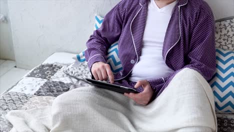 man in pajamas using tablet in bed