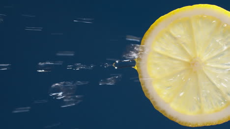 vertical of slow motion macro shot of flowing water from lemon slice on blue-black background