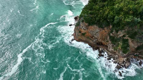 orbit drone shot of rocky cliff and adriatic sea with waves crashing during the day in montenegro