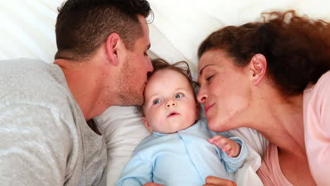 niño en azul babygro con padres felices en la cama
