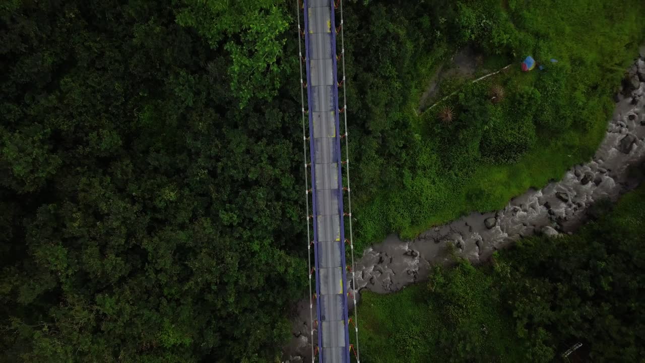 Ripresa aerea di un ponte sospeso in metallo che attraversa una valle e un fiume con cascata.