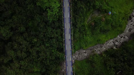 Aerial-shot-of-metal-suspension-bridge-build-in-the-crossing-of-the-valley-and-river-with-waterfall