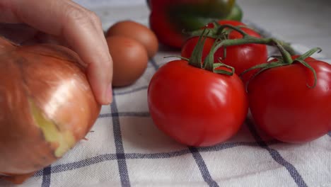 putting ripe red tomatoes and golden onion on a table with eggs and bell pepper to cook a dish