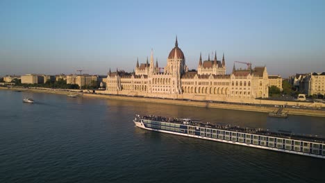 drone orbits above boat on danube river with hungarian parliament in background