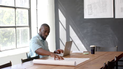 architect working on blueprints and using laptop in modern office