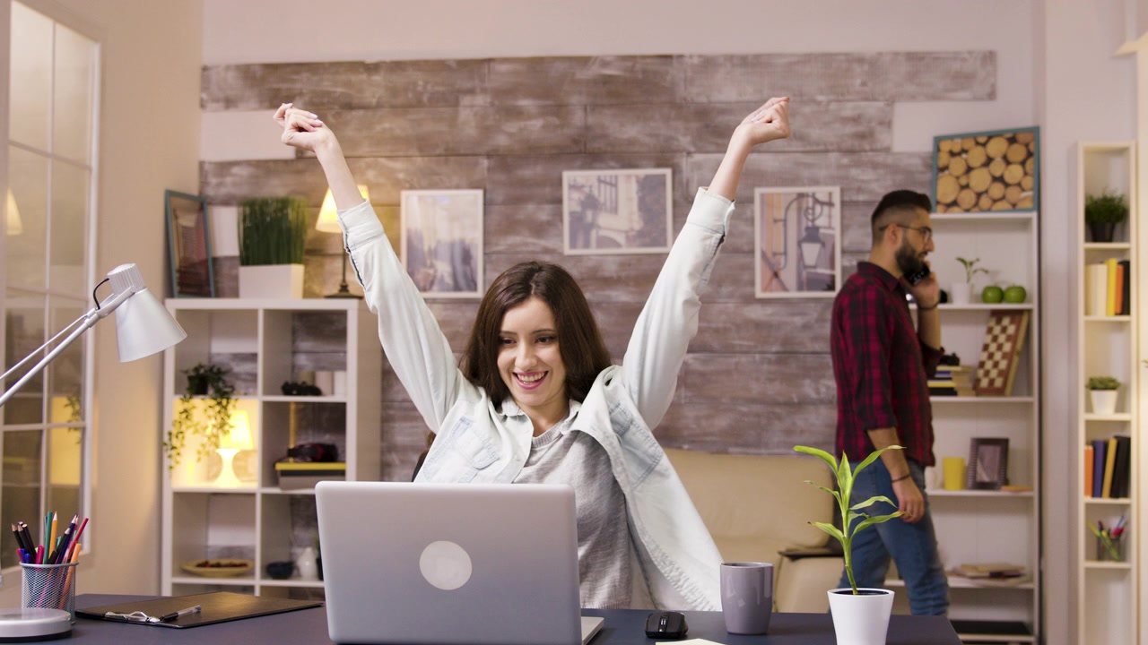 Giovane donna che celebra il successo mentre lavora al laptop nell'ufficio di casa