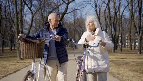 senior couple holding bikes while walking and talking in the park on a winter day