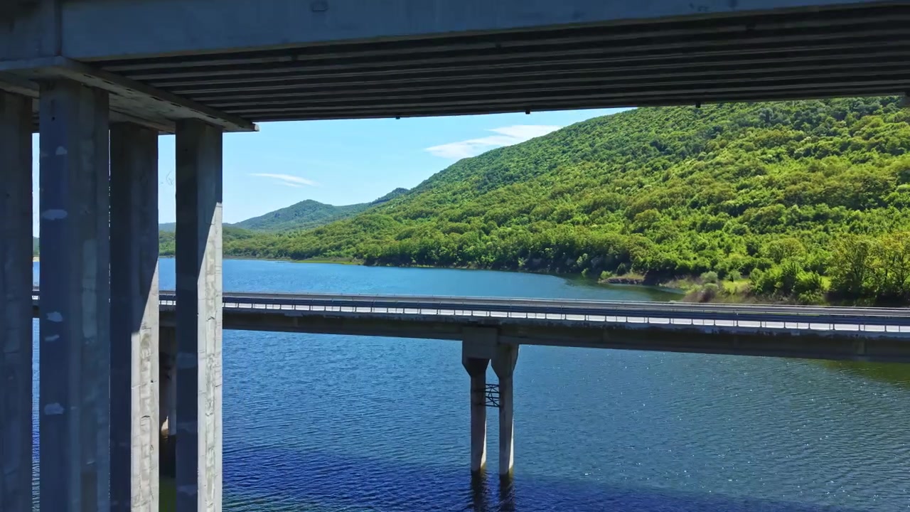夏の晴れた日、緑の丘に囲まれた湖に橋がかかっている。