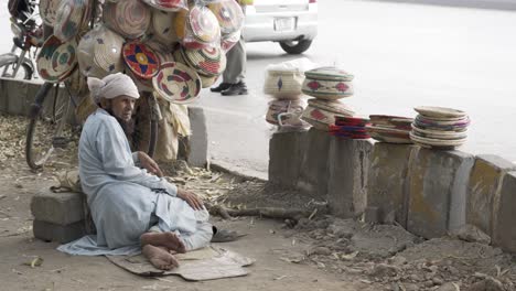 a shot captured an elderly gentleman seated along a street, calmly awaiting potential buyers for his valuable handicrafts.