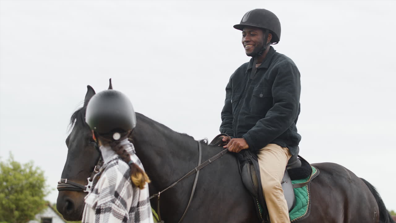hombre sonriente montando caballo negro y hablando con una mujer joven caminando junto a él