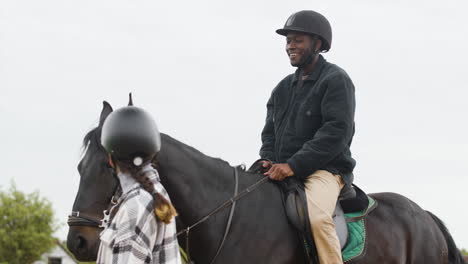 smiling man riding black horse and talking with young woman walking next to him