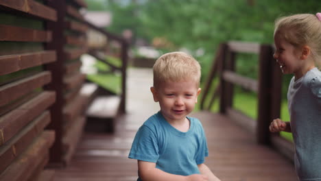 Little-girl-runs-playing-with-funny-brother-on-veranda-deck