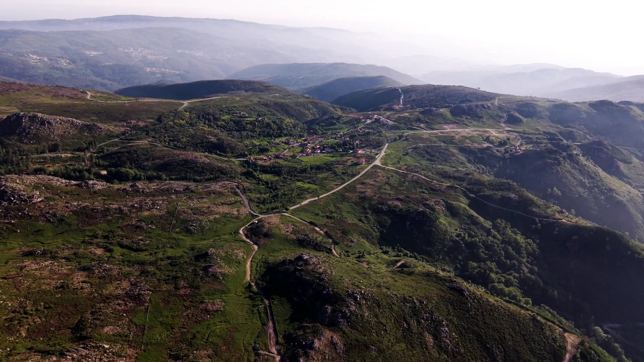 Una strada sterrata si snoda oltre un villaggio collinare attraverso la valle di montagna nella Serra da Freita in Portogallo