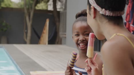 Happy-african-american-mother-and-daughter-eating-ice-cream-by-swimming-pool,-slow-motion