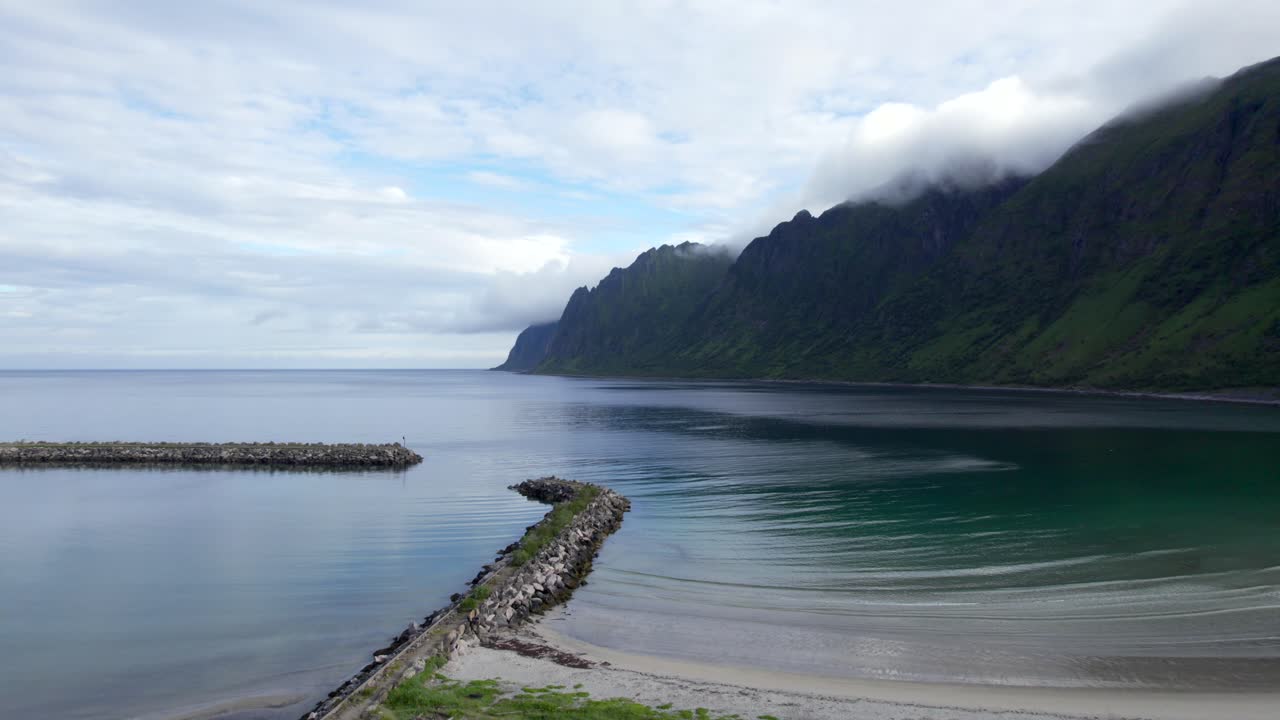 Flying sideways over Ersfjord Beach on Senja with clouds crawling over the mountain