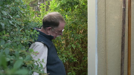 man paints wooden shed outside of house, inspecting his work