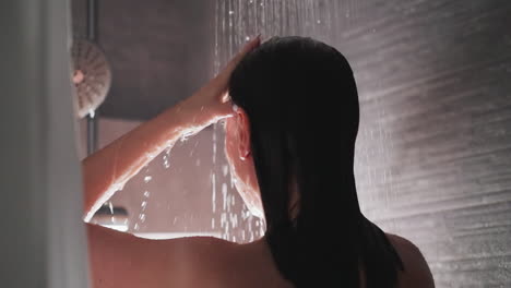 woman shampooing hair under contemporary shower. lady rinsing hair under modern shower at residence. brunette makes cleansing routine washing hair