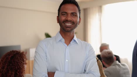 indian business man smiling on camera while working with colleagues inside bank office