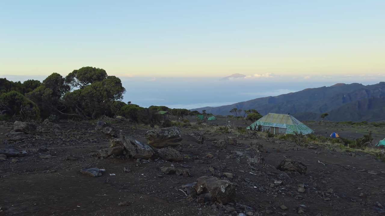 Open rocky plateau on Mount Kilimanjaro with soft sky and rugged volcanic terrain, establishing pan at campsite
