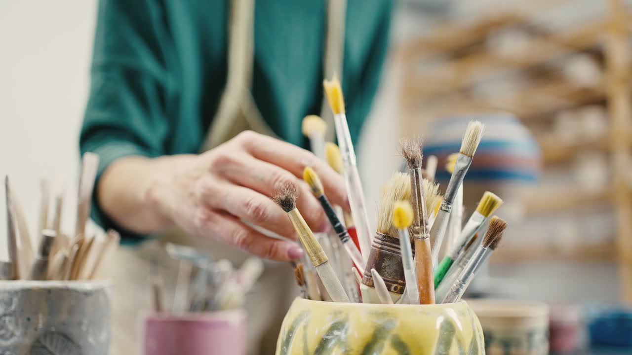 fotografía de cerca de una artista mujer eligiendo un pincel para la decoración de la cerámica, en cámara lenta