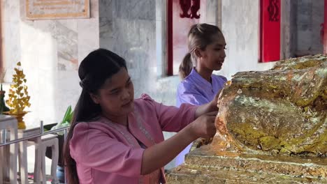 applying gold leaf to a statue in a thai temple