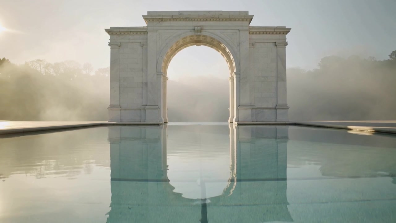 Uno specchio d'acqua increspato riflette un arco in pietra su una terrazza, mentre una leggera brezza e il sole disperdono la nebbia.