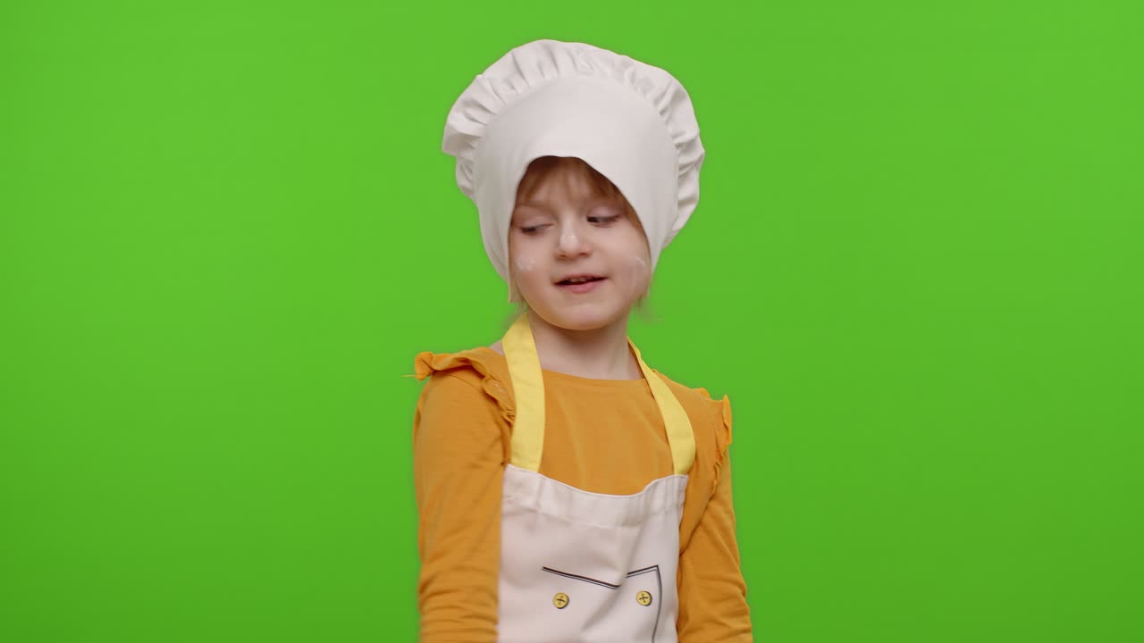 Bambina divertente vestita da cuoca/chef/fornaia con grembiule e cappello che balla, scherza e fa smorfie