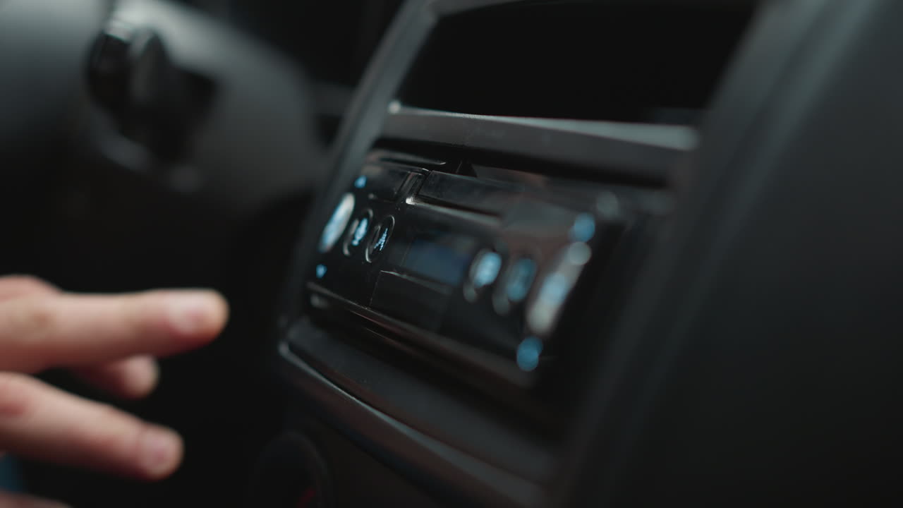 Hand of driver pressing button on music player control panel in car console interior with focus on finger gesture and knob detail under ambient lighting for audio adjustment showcasing dashboard trim