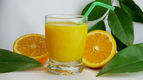 close up studio shot of full glass of orange juice and orange halves, fast pan