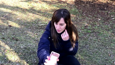 slowmo of young girl taking selfies with a smartphone using front camera sitting on the ground in a urban park