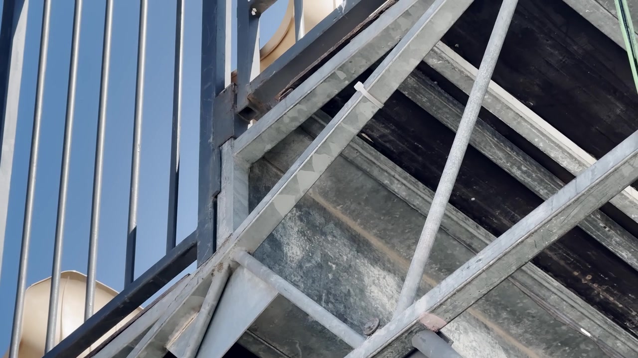 Close-up of steel support beams and vertical railings under tennis court stands, showing grandstand framework, metal bracing, and sports venue construction detail.