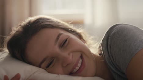 Blonde-woman-waking-up-in-sunny-day-in-bed-and-looking-at-camera