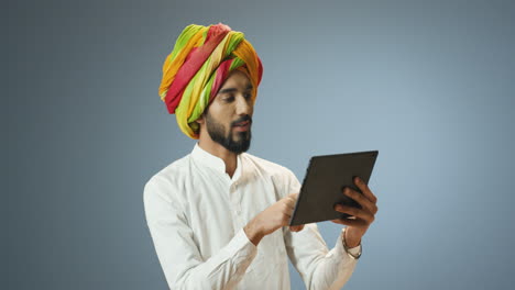 Young cheerful Indian man in traditional clothes and turban making a video call using a tablet