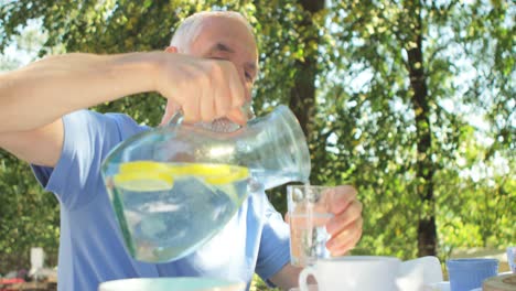 senior man pouring water in glass at garden