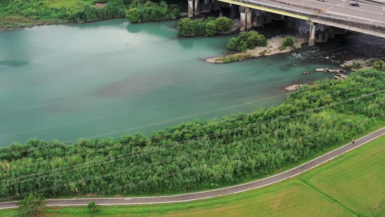 4K aerial drone footage of river landscape with greenery, cycling path, and a man walking, infrastructure in harmony