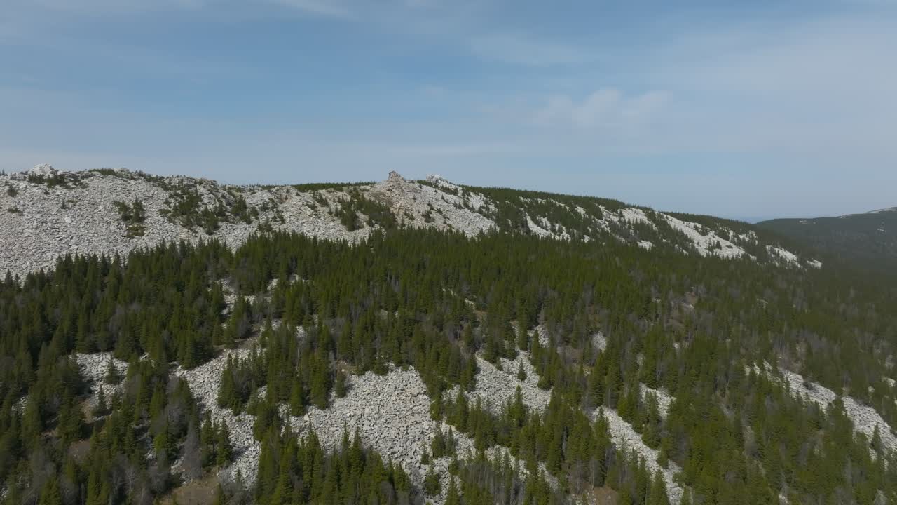 Droneoptagelse af en klippefyldt bjergryg dækket af taiga-nåleskov under en klar blå himmel i Zyuratkul Nationalpark, Tjeljabinsk oblast, Rusland