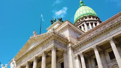 slow motion low angle view of national congress of argentina, national flag waves over summer skyline in buenos aires city historical landmark