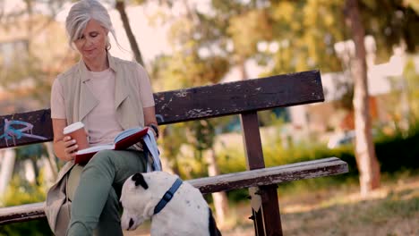 mature woman with dog and coffee reading book in park