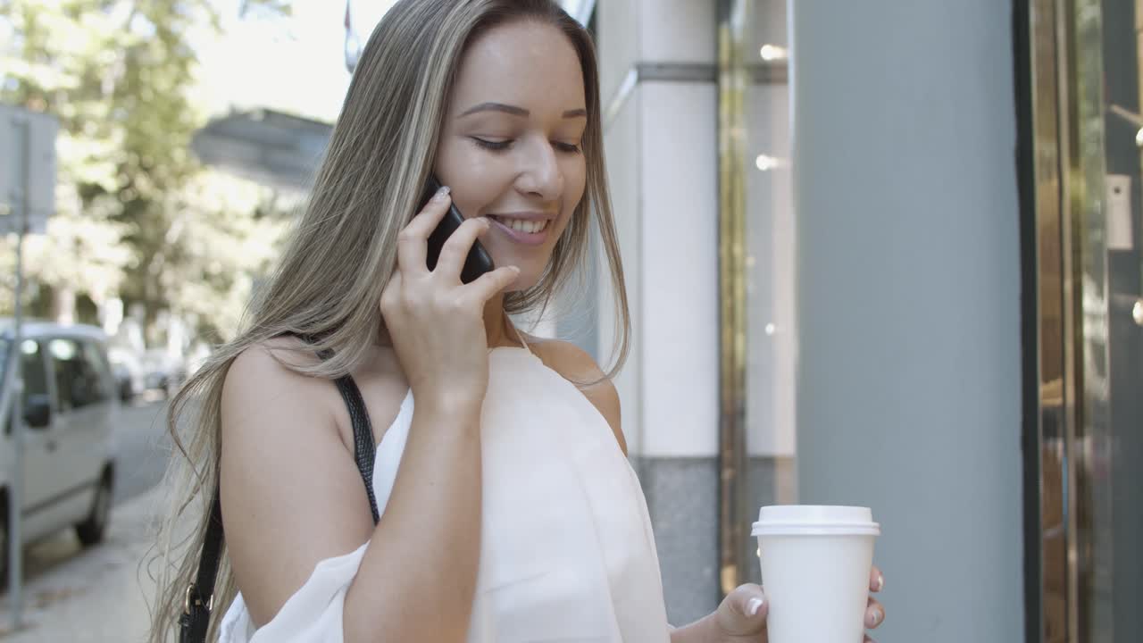 긴 머리 금발의 여자가 거리에 서서 전화 통화