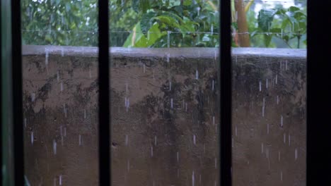 una toma en cámara lenta desde dentro de una habitación cerrada con barras mirando la lluvia torrencial en un recinto amurallado con alambre de púas