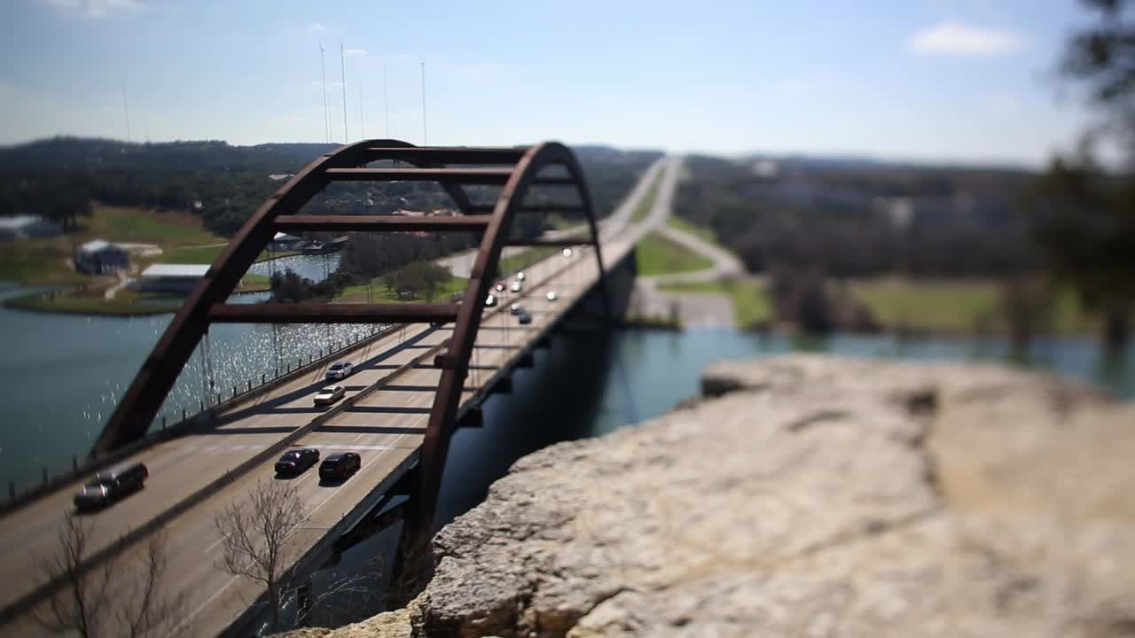 Austin Pennybacker Bridge, focus tilted to highlight narrow segment of ledge - front part of bridge. Couple moves onto ledge to enjoy the view - the man points towards downtown.