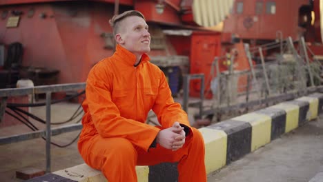 young man in orange uniform sitting during his break by the sea in the harbor