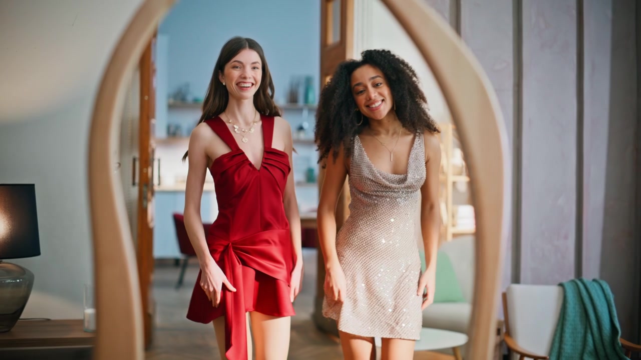 To kvinder i aftenkjoler står foran spejlet og nyder deres outfits. Multietniske veninder