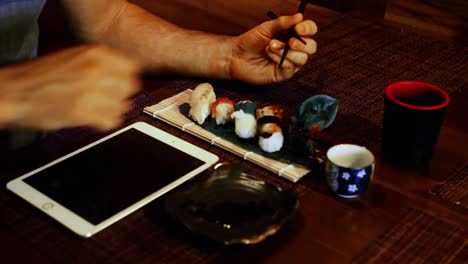 man using digital tablet while having sushi in restaurant