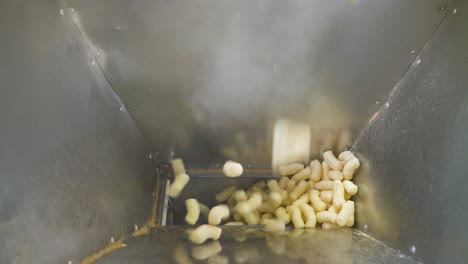 yellow corn sticks falling down into a metal container. automatic production of snacks in a food factory