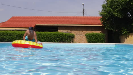 male model riding a inflatable floatie in a outdoor swimming pool during summer.